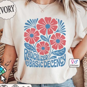 May include: Ivory-colored unisex t-shirt with a floral design in red and blue. The graphic includes the text "RADICALIZED BY BASIC DECENCY". The shirt is customizable and made of Comfort Colors 1717 material.