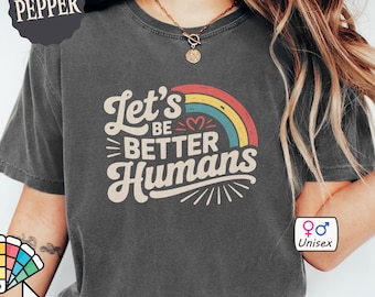 Könnte beinhalten: Dunkelgraues Unisex-T-Shirt mit dem Text "Let's Be Better Humans" über einer Regenbogen-Grafik. Das Shirt ist anpassbar und aus Comfort Colors 1717 Material. Das Shirt ist unisex.