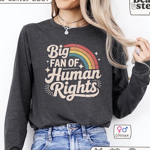 May include: Dark gray long-sleeve shirt with the text "Big Fan of Human Rights" in a retro design. The graphic includes a rainbow and stars. The shirt is unisex.