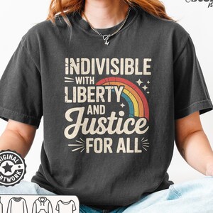 May include: Dark gray t-shirt with the words "INDIVISIBLE WITH LIBERTY AND JUSTICE FOR ALL" in white and a rainbow graphic. The shirt also has a "ORIGINAL ARTWORK" logo.