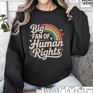 May include: Black unisex sweatshirt with the text "Big Fan of Human Rights" in a retro font, with a rainbow graphic. The sweatshirt is a Gildan 18000 model.