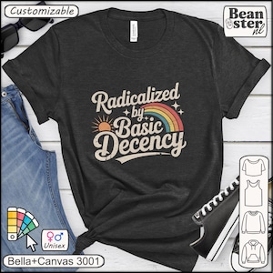 Op de afbeelding: Donkergrijs unisex T-shirt met de tekst "Radicalized by Basic Decency" in een retro lettertype, met een regenboog en zon grafiek. Het shirt is gemaakt van Bella+Canvas 3001 materiaal.