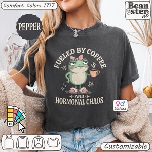 Pu&ograve; includere: T-shirt unisex grigio scuro con grafica a rana con tazza di caff&egrave;. Il testo recita "Fueled by Coffee and Hormonal Chaos". La maglietta &egrave; personalizzabile e realizzata in materiale Comfort Colors 1717. Il colore &egrave; Pepper.