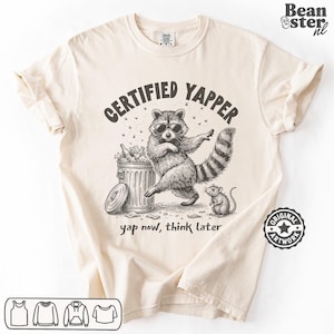 May include: Cream-colored t-shirt with a graphic of a raccoon wearing sunglasses, standing next to a trash can. The text "CERTIFIED YAPPER" is above the raccoon, and "yap now, think later" is below. A small mouse is also in the image.