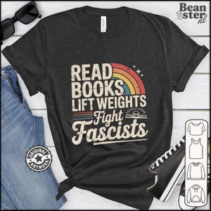 May include: A dark grey t-shirt featuring the slogan "READ BOOKS LIFT WEIGHTS FIGHT FASCISTS" in a retro style with a rainbow and stars. The shirt is displayed with blue jeans and black sunglasses.
