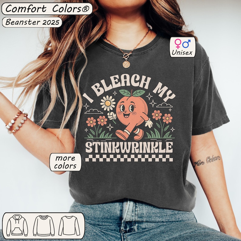 May include: A dark gray t-shirt with a graphic of a peach with a face and the text "I bleach my stinkwrinkle". The peach is holding a flower. The text is in a retro font.