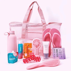 May include: A collection of pink summer essentials, including a mesh tote bag, water bottle, flip-flops, a portable fan, sunscreen, hand cream, and a hairbrush. Other items include lip balm, hair clips, and face mask packets.