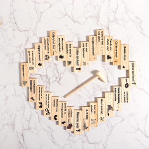 May include: A heart-shaped arrangement of small wooden blocks with various French phrases and illustrations, along with a wooden mallet. The blocks are arranged on a marble-patterned surface.