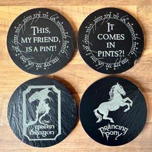 May include: Four black slate coasters with white text and images. The coasters feature the text "This, my friend, is a pint!" "It comes in pints?!" and images of a prancing pony and a green dragon.