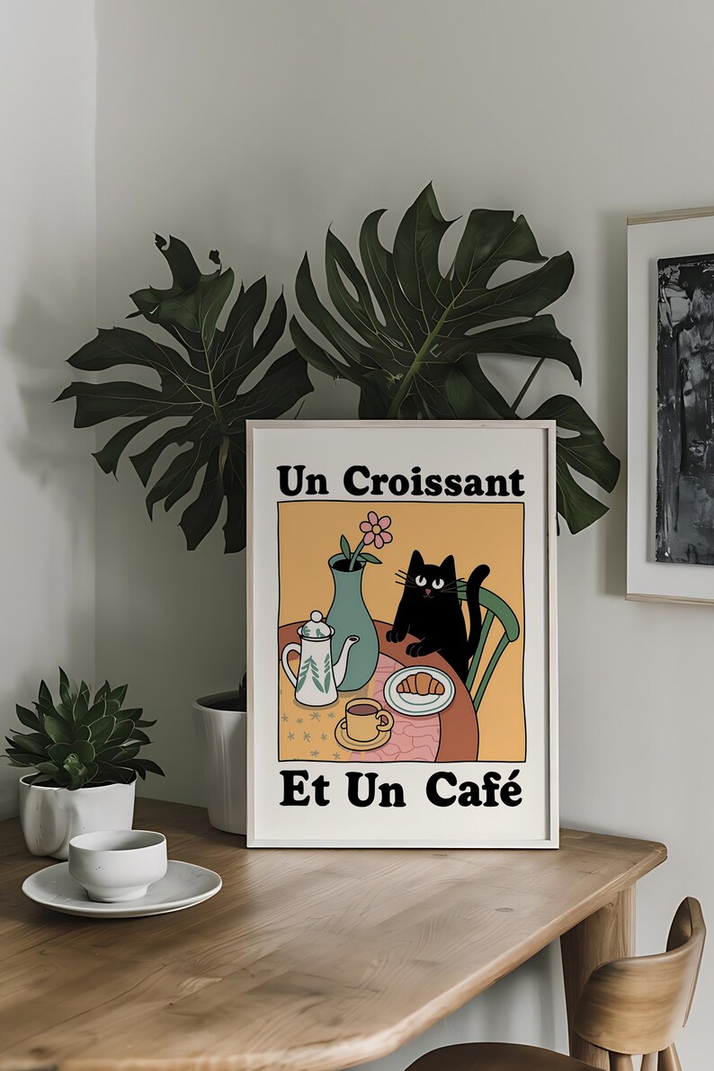 May include: A white framed print with a black cat sitting at a table with a croissant, a cup of coffee, and a teapot. The text on the print reads "Un Croissant Et Un Caf&eacute;".