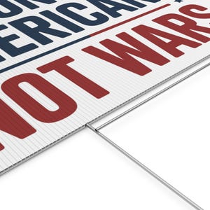 May include: White yard sign with the text "NOT AMERICAN WARS" in red and navy blue. The sign has a corrugated plastic surface and a metal stake for ground placement.
