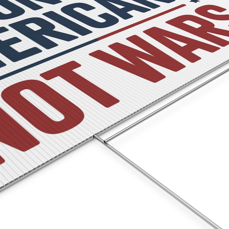 May include: White yard sign with the text "NOT AMERICAN WARS" in red and navy blue. The sign has a corrugated plastic surface and a metal stake for ground placement.