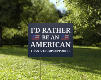 May include: A blue and white yard sign with the text "I'd rather be an American than a Trump supporter". The sign features two small American flags.