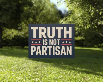 May include: A dark blue yard sign with the words "TRUTH IS NOT PARTISAN" in white lettering and red and white stripes and stars. The sign is displayed on a metal stake in a grassy yard with trees in the background.