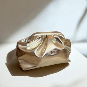 Peut inclure: Une pochette de soirée en métal doré avec un design plissé et plissé. Le sac a une poignée supérieure et un petit logo doré sur le devant.