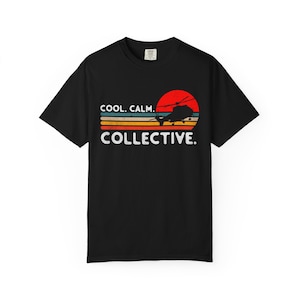 May include: A black short-sleeve t-shirt featuring a graphic of a helicopter silhouette against a red sun and horizontal stripes in yellow, orange, and blue. The text COOL. CALM. COLLECTIVE. is printed in white below the graphic design.