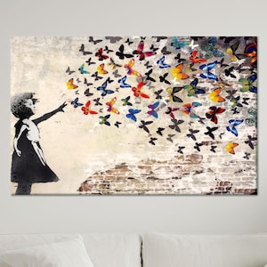 May include: A canvas print featuring a black and white silhouette of a girl releasing colorful butterflies. The butterflies are in shades of red, yellow, blue, and green, set against a textured, off-white background with a brick wall.
