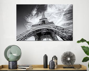 以下が含まれることがあります： フランスのパリにあるエッフェル塔の白黒写真。写真は低い角度から撮影されており、塔を見上げています。空は曇っていて、塔は雲を背景にシルエットになっています。