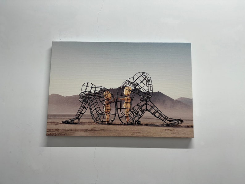 May include: A black metal sculpture of three figures in a desert landscape. The figures are posed in a way that suggests they are embracing or protecting each other.