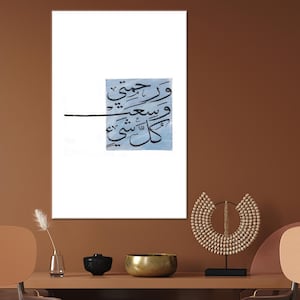 May include: An art print with Arabic calligraphy in black on a light blue square, set against a white backdrop. The print is displayed on a brown wall. A table below holds decorative items, including a wooden sculpture.
