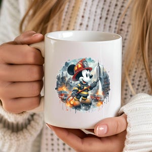 May include: White ceramic mug with a colorful illustration of Mickey Mouse dressed as a firefighter holding a hose. The illustration is surrounded by a watercolor-style background with buildings and flames.