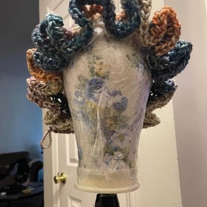 May include: A crocheted hairpiece with a variety of colors, including blue, pink, and brown. The hairpiece is made of yarn and is designed to be worn on the head.
