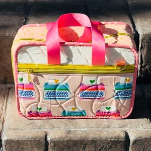 May include: A pink and yellow quilted bag with a typewriter pattern. The bag has a bright pink handle and a gold zipper. The typewriter pattern includes typewriters in blue, pink, and green with a green heart above each typewriter.
