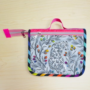 May include: A square, zippered pouch with a pink handle and zipper pull. The pouch features a gray and white illustration of a leopard amidst floral branches. The edges are trimmed with a rainbow stripe.