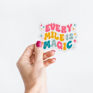May include: A white sticker with the text "Every Mile is Magic" in colorful, bubbly letters. The sticker has a white background and is decorated with small, colorful stars.