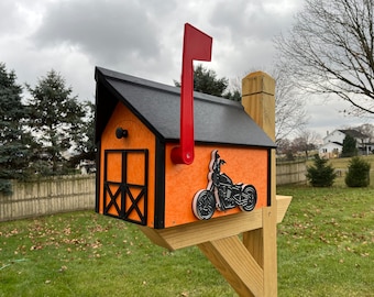 May include: Orange and black mailbox with a black motorcycle silhouette on the front. The mailbox has a black roof and a red flag.