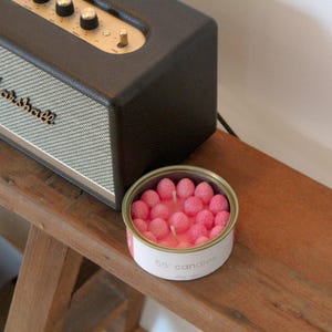 Peut inclure: Une bougie rose dans un récipient en étain avec le texte "55° candles" sur l'étiquette. La bougie est faite de petites pièces de cire rose en forme de fraise.
