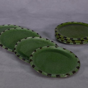 Peut inclure: Ensemble de six assiettes en céramique verte avec une bordure noire. Les assiettes sont de forme ovale et ont un glaçage moucheté.