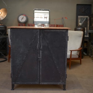 Peut inclure: Une armoire en métal noir avec deux portes. L'armoire a un dessus en bois et se trouve sur un sol en bois.