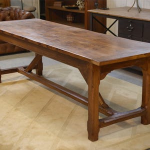 May include: A rectangular wooden dining table with a natural brown finish, featuring a smooth flat top surface, four sturdy straight legs, and a central horizontal support beam connecting the legs with angled braces for structural stability.