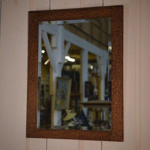 Peut inclure: Un miroir rectangulaire avec un cadre texturé de couleur cuivre. Le miroir reflète une pièce avec des poutres blanches et divers objets. Le cadre a un aspect martelé, ajoutant une touche rustique au décor.