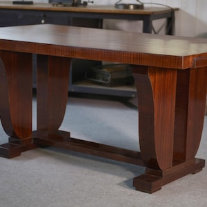 May include: A rectangular, dark brown wooden table with a polished finish. The table has a solid top and is supported by four curved legs, connected by a lower stretcher. The table is approximately 183 cm long.