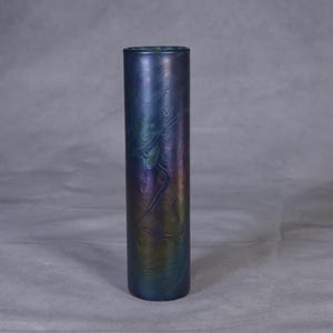 Puede incluir: Un jarrón de vidrio cilíndrico y alto con un acabado iridiscente azul, morado y verde. El jarrón tiene una superficie texturizada con un patrón de remolino.