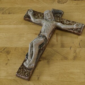 Peut inclure: Une croix murale religieuse représentant Jésus-Christ. La croix est faite d'un matériau brun foncé avec une surface texturée. La figure est peinte dans des tons de gris et de blanc. Un objet décoratif.