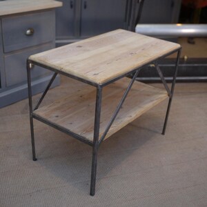 Könnte beinhalten: Ein kleiner, zweistufiger Beistelltisch mit einer rustikalen Holzplatte und einem schwarzen Metallrahmen. Der Tisch hat ein schlichtes, industrielles Design.