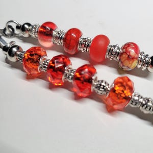 May include: A silver charm bracelet with red and orange glass beads. The bracelet has a lobster clasp and is made of metal.