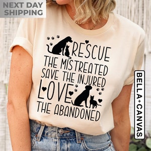 May include: A beige t-shirt with a black graphic design featuring a dog and cat with the text "Rescue the mistreated, save the injured, love the abandoned".