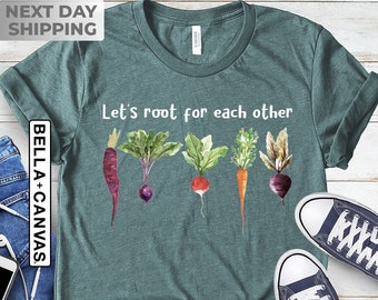 May include: A teal green t-shirt with the text "Let's root for each other" and a watercolor illustration of five vegetables. The vegetables are a carrot, a beet, a radish, a turnip, and a green onion.