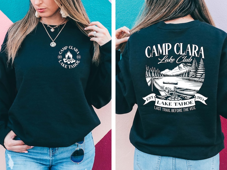 May include: Black sweatshirt with a white graphic on the front that says "Camp Clara Lake Tahoe" and a white graphic on the back that says "Camp Clara Lake Club" with a scene of a lake, mountains, and trees. The text on the back also says "Est. 2024" and "Last Trail Before The Veil."