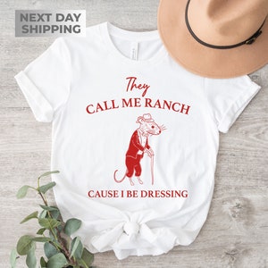 May include: White t-shirt with a red graphic of a mouse wearing a tuxedo and holding a cane. The text "They Call Me Ranch Cause I Be Dressing" is printed in red below the mouse.