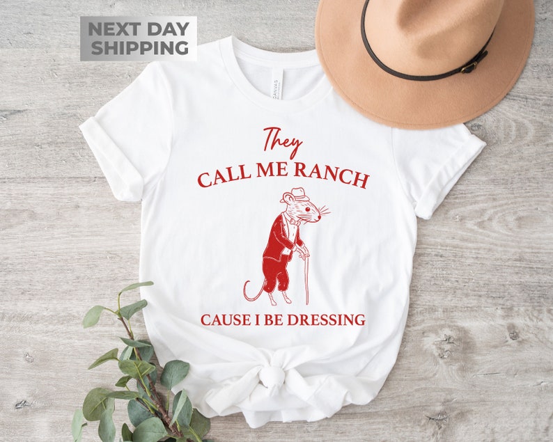 May include: White t-shirt with a red graphic of a mouse wearing a tuxedo and holding a cane. The text "They Call Me Ranch Cause I Be Dressing" is printed in red below the mouse.