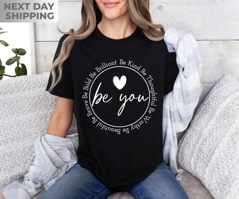 May include: Black t-shirt with a white circle graphic that says "be you" with a heart and the words "Be Kind Be Thoughtful Be Worthy Be Brilliant Be Beautiful Be Brave Be Bold" around the circle.