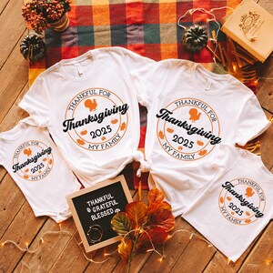 May include: White t-shirts with a Thanksgiving design. Each shirt displays a circular graphic with a turkey, the text "Thankful for Thanksgiving 2025 My Family", and autumn leaves. A small chalkboard reads "Thankful, Grateful, Blessed".