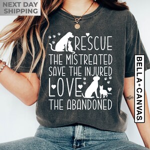 May include: A dark gray t-shirt with a white graphic design featuring a dog and cat silhouettes. The text reads "Rescue the mistreated, save the injured, love the abandoned".