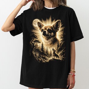 May include: Black t-shirt featuring a detailed illustration of a Chihuahua dog with a radiant glow, a full moon, and a forest scene. The design includes a smaller dog silhouette on a rock, creating a nature-inspired theme.