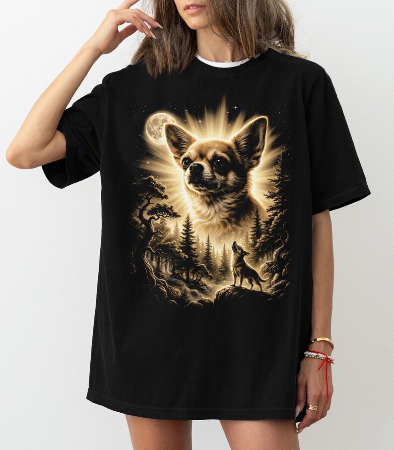 May include: Black t-shirt featuring a detailed illustration of a Chihuahua dog with a radiant glow, a full moon, and a forest scene. The design includes a smaller dog silhouette on a rock, creating a nature-inspired theme.